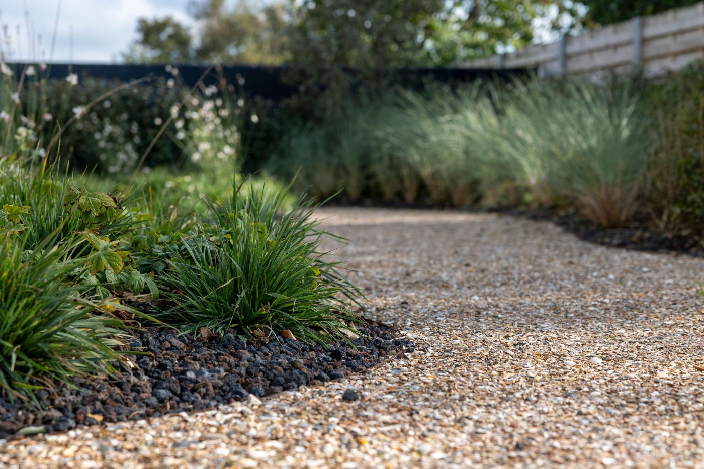 Kronkelend grindpad met kleurrijke beplanting, omringd door een houten omheining.