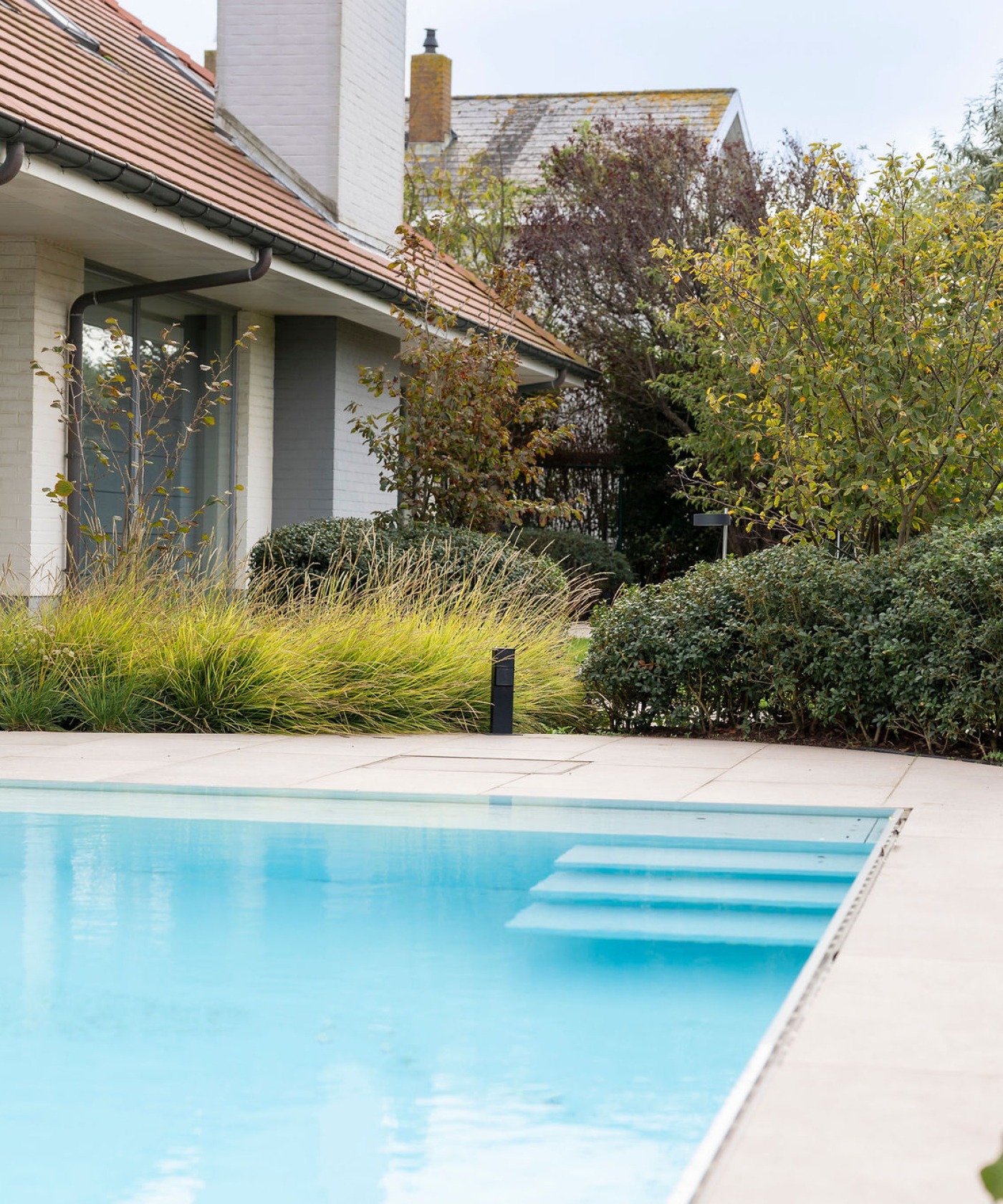 Luxe tuin met zwembad en bloeiende borders, harmonieus ingepast in de omgeving.