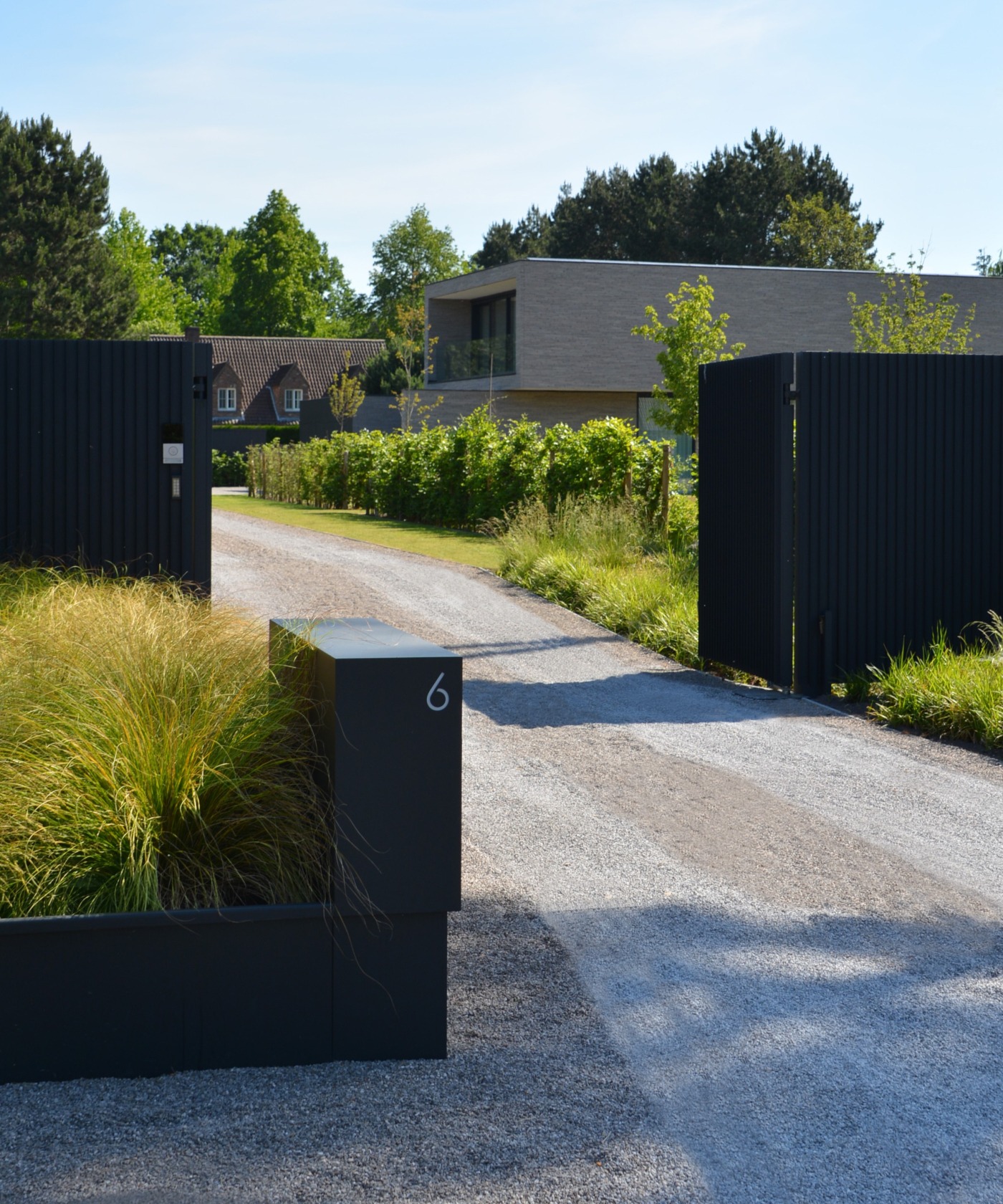 Moderne villa met strakke, minimalistische tuinarchitectuur, oprit en toegangspoort voor extra privacy.