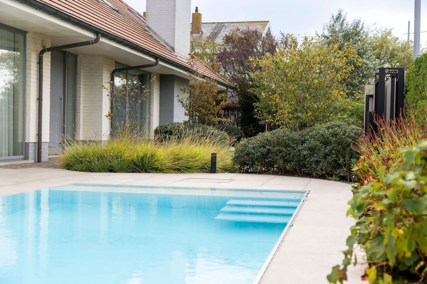 Luxe tuin met zwembad en bloeiende borders, harmonieus ingepast in de omgeving.