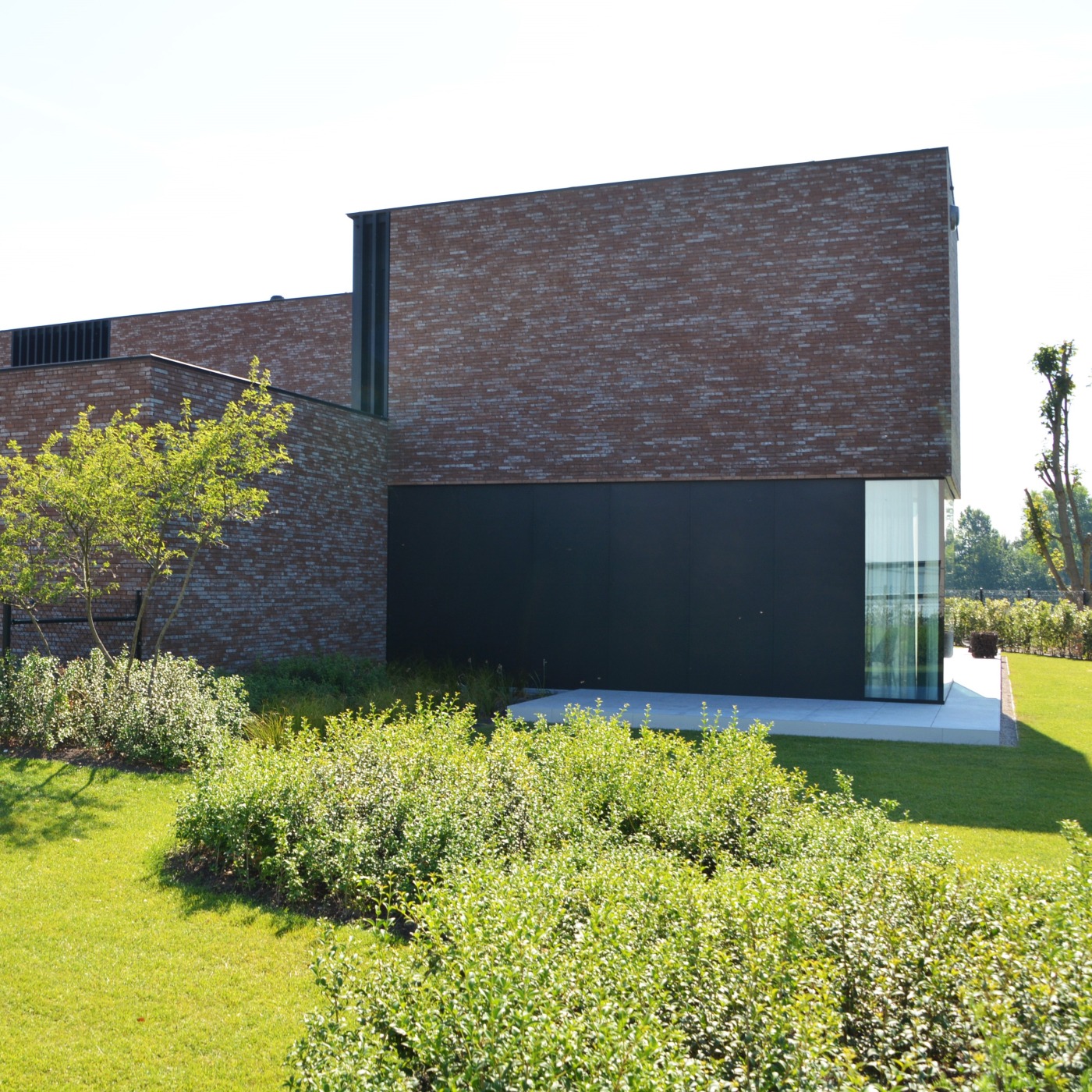 Moderne villa in Eke met strakke lijnen, omgeven door groenblijvende beplanting en meerstammige bomen.