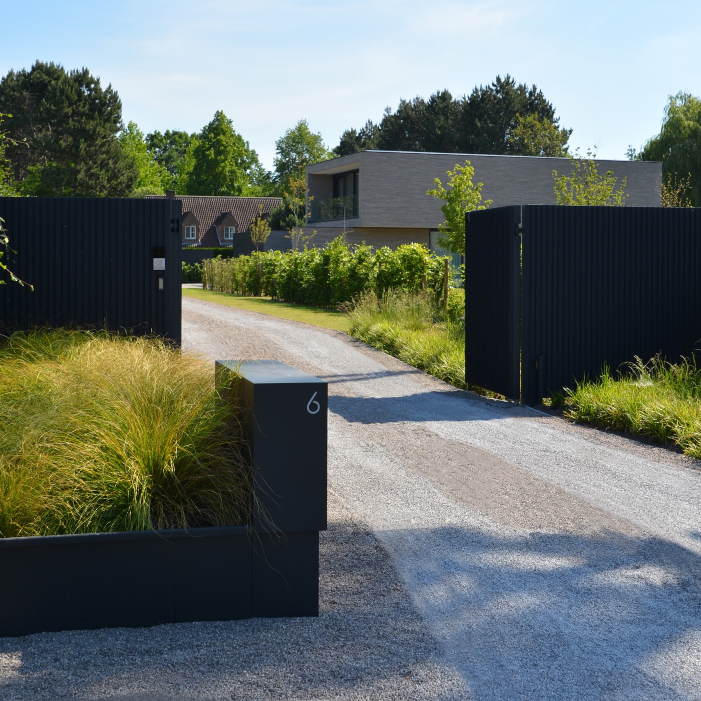 Moderne villa met strakke, minimalistische tuinarchitectuur, oprit en toegangspoort voor extra privacy.